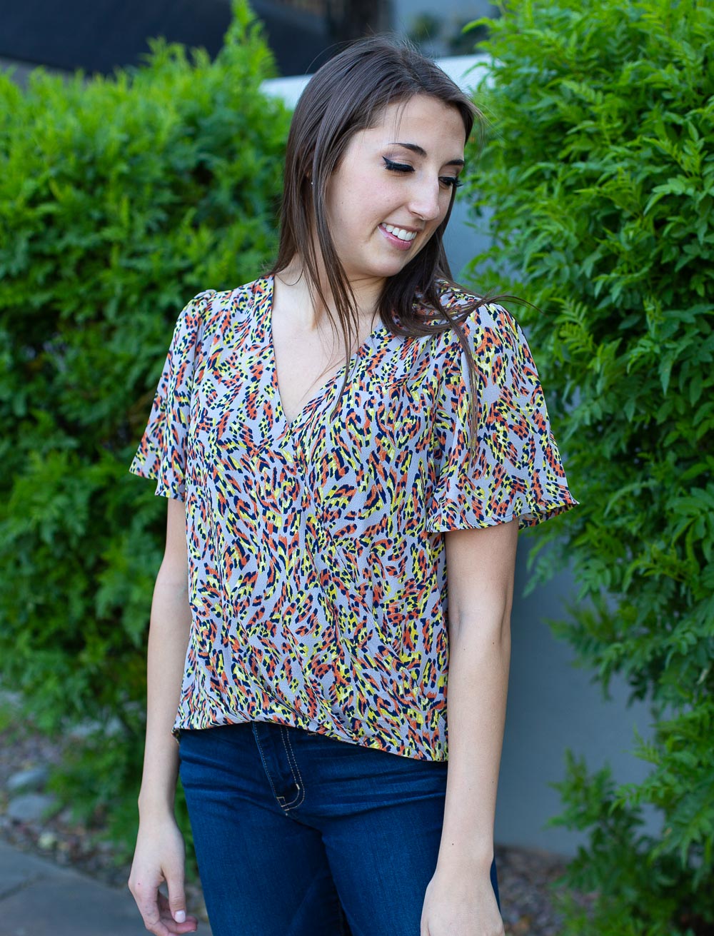 Cross front wrap top with high-low hemline, flutter sleeves and colorful abstract print